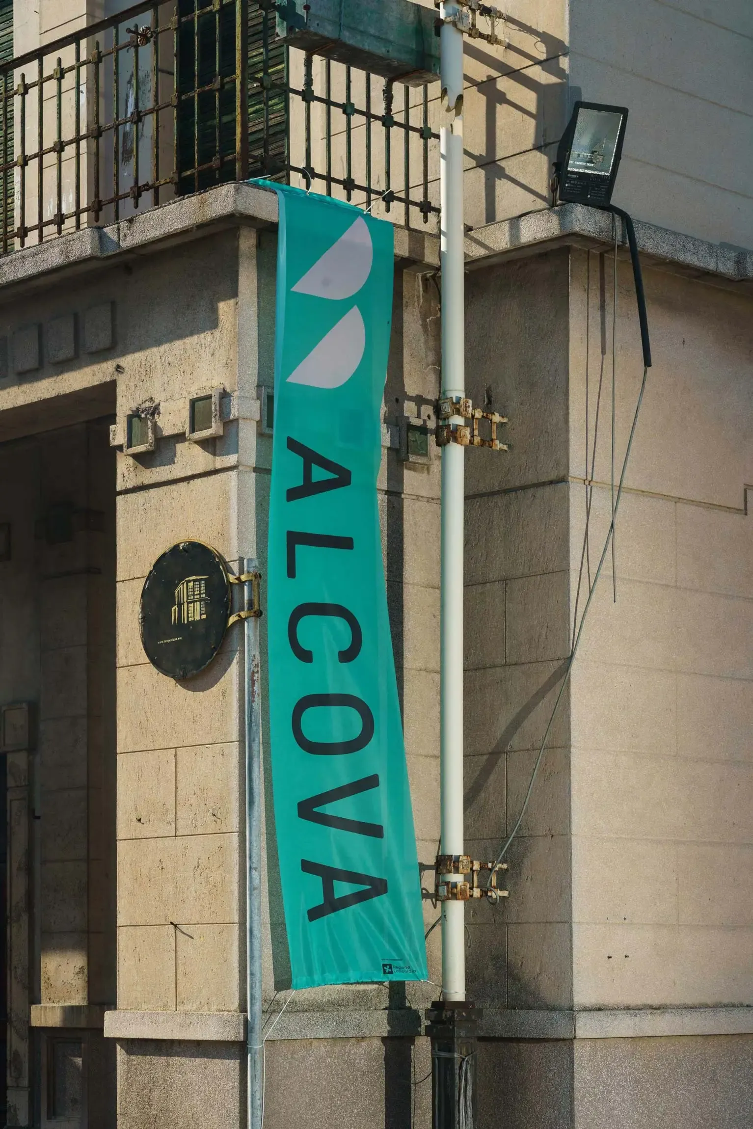 Vertical Alcova banner in green with black lettering, displayed on the exterior wall of the former Porta Vittoria Abattoir building in Milan. | Carlotta Bacchini