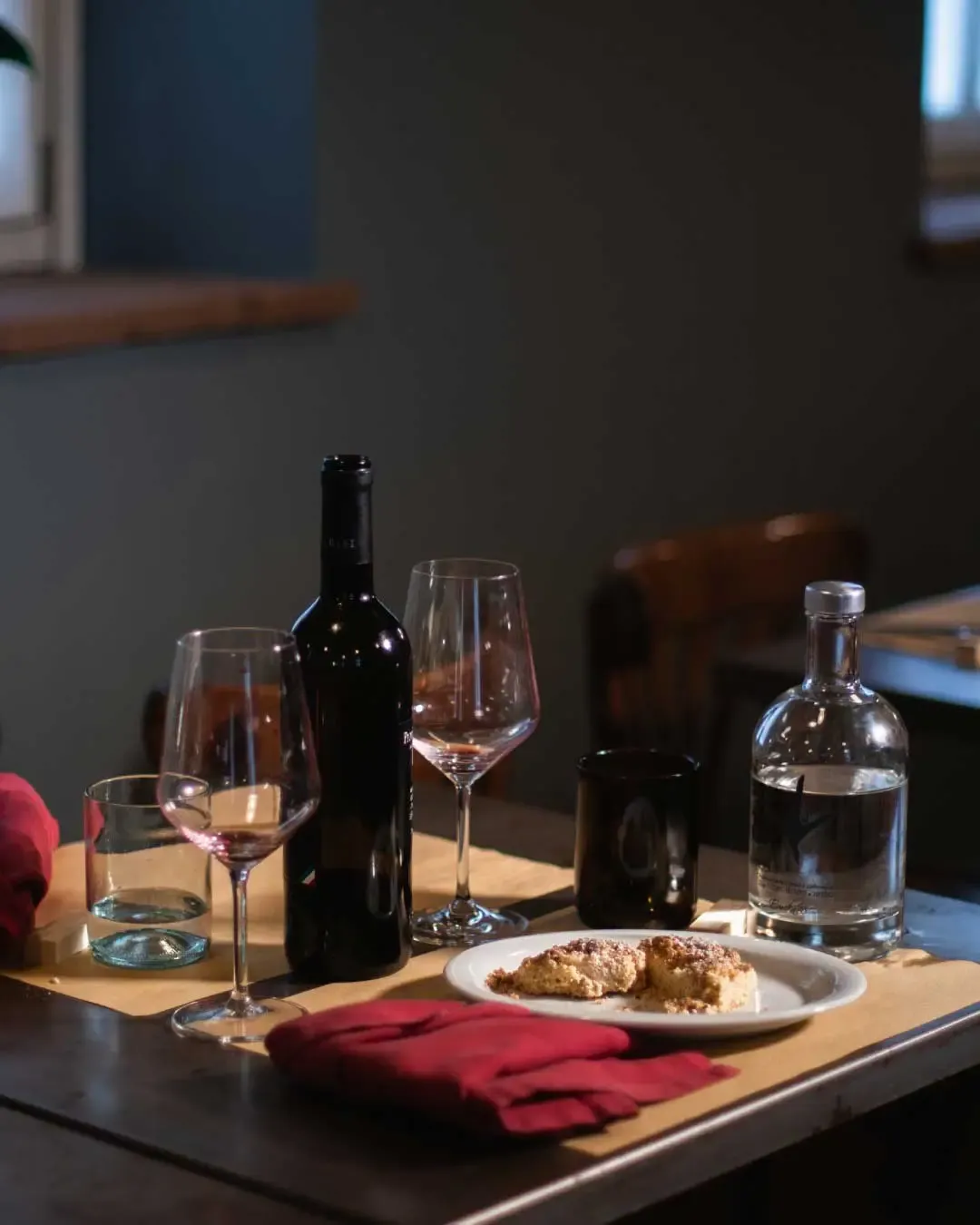 Close-up of a restaurant table set with red napkins, wine glasses, a wine bottle, a water bottle, and a dessert plate at Osteria del Gallo Ardito | Carlotta Bacchini