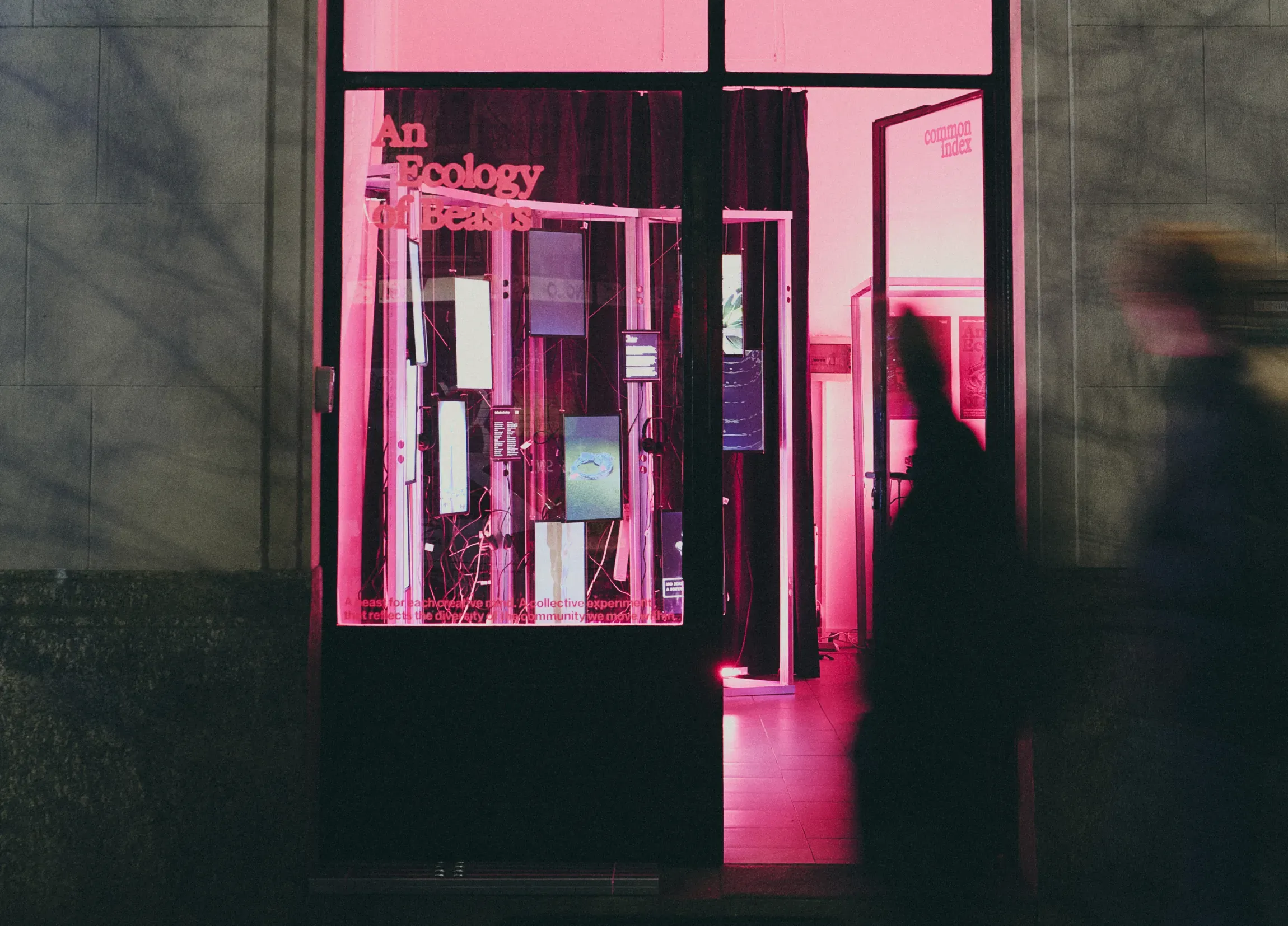 An Ecology of Beasts collective design exhibition at TXT Studio Milan, storefront installation with multiple vertical screens and pink lighting | Carlotta Bacchini