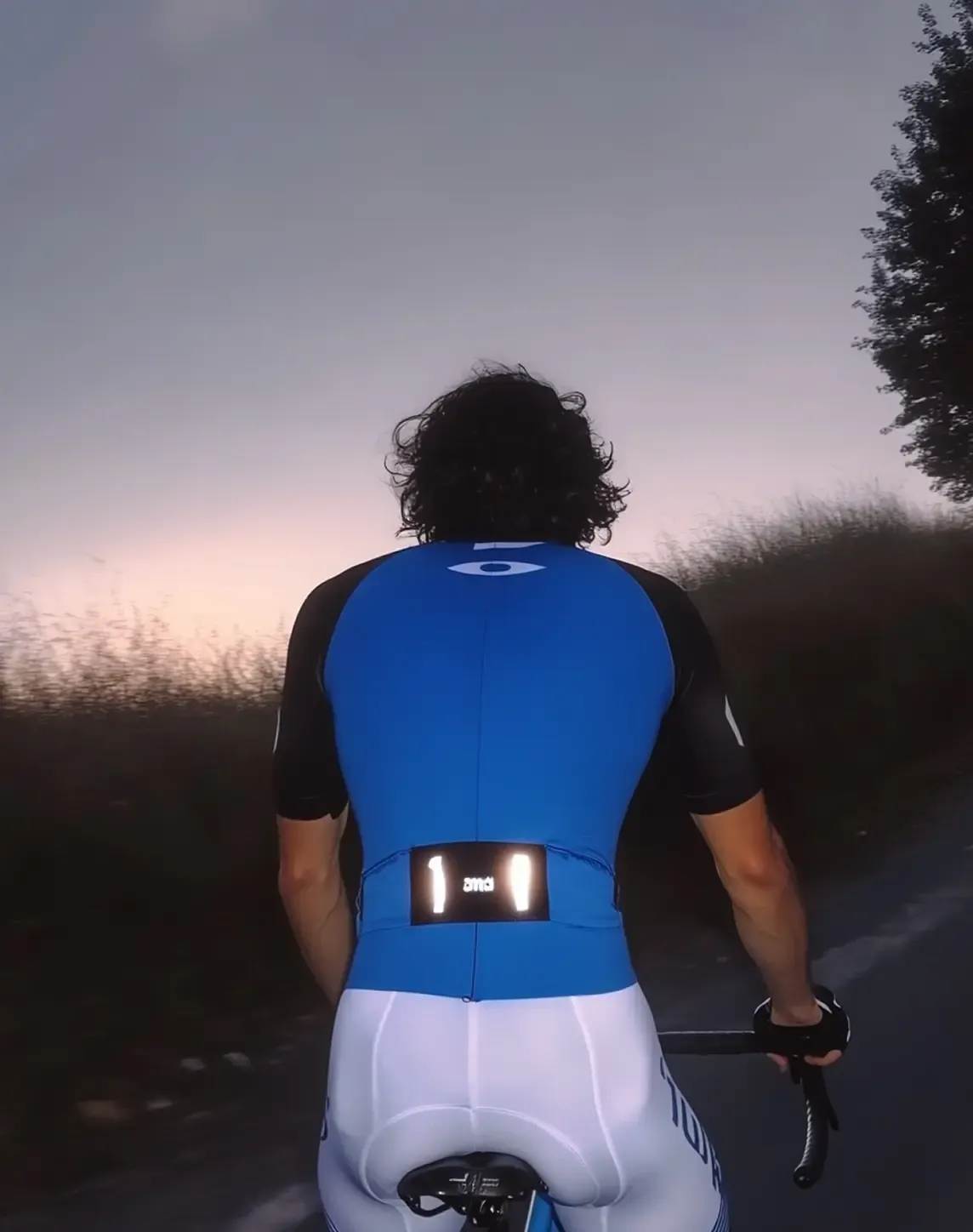 AI-generated fashion image of an urban cyclist riding at dusk, wearing a blue cycling kit with reflective details.
