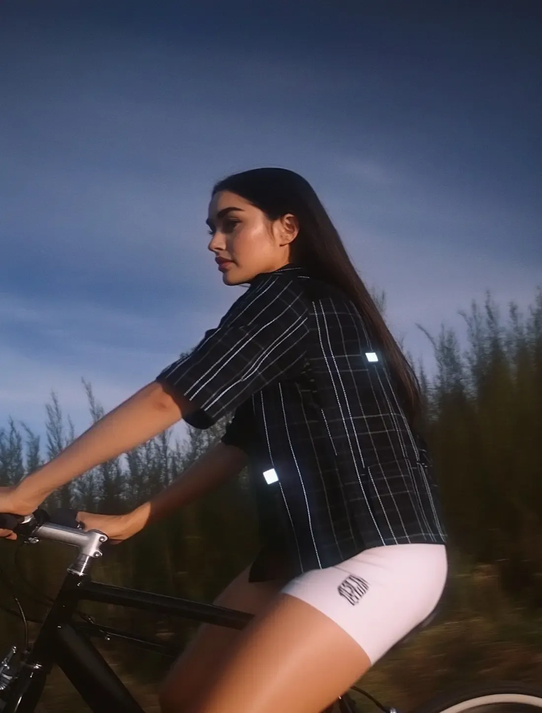 AI-generated fashion image of a female urban cyclist riding at sunset, wearing a striped shirt and white cycling shorts.